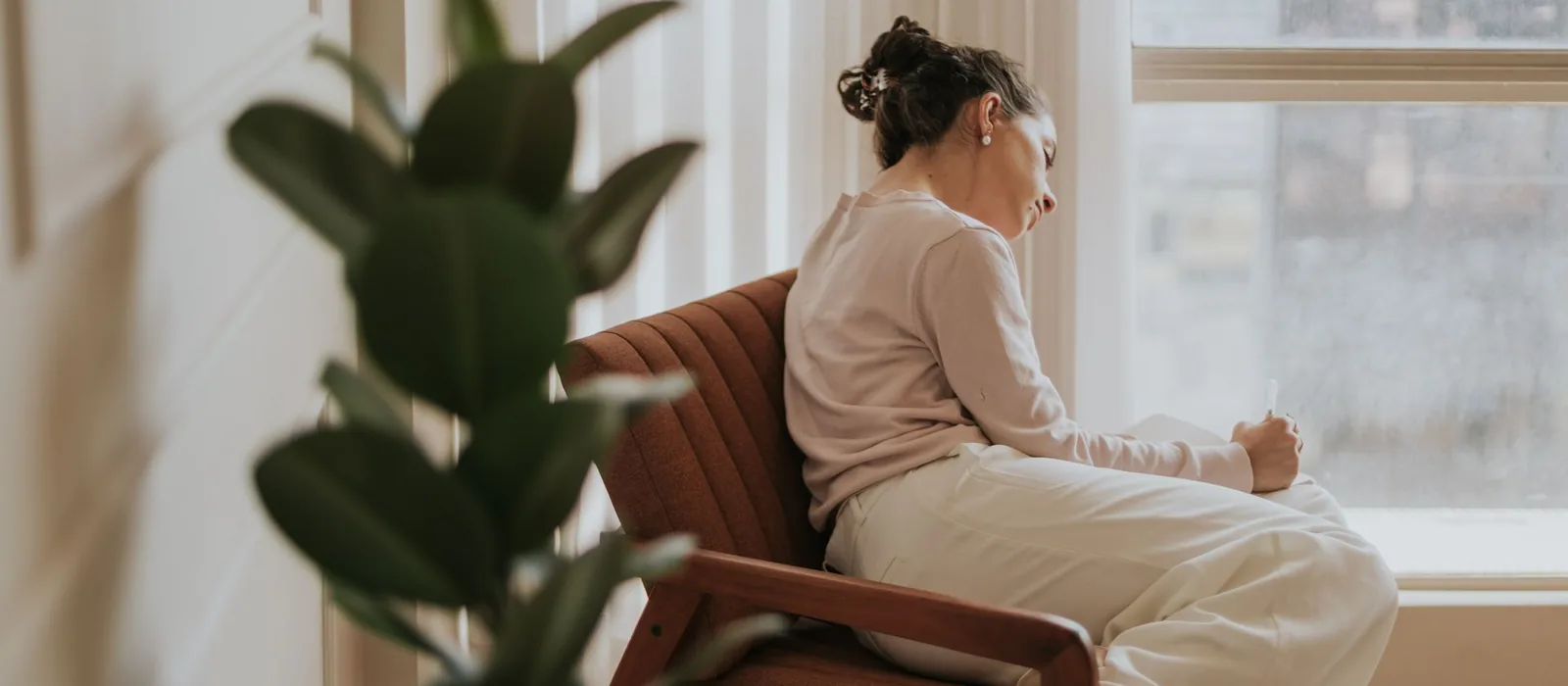 A woman sitting quietly in a chair by a window